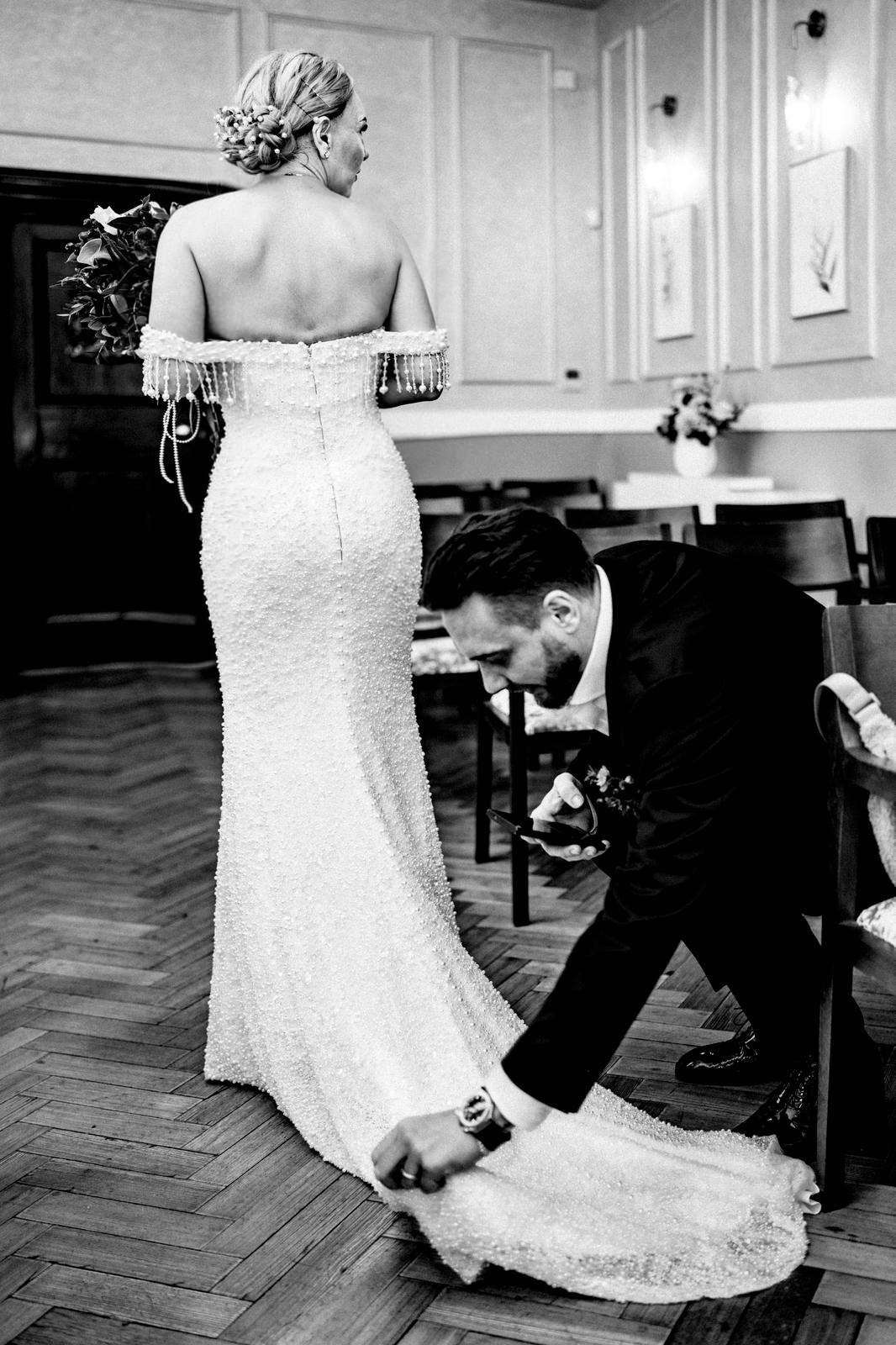 Attentive groom adjusts the bride's stunning beaded wedding gown train.