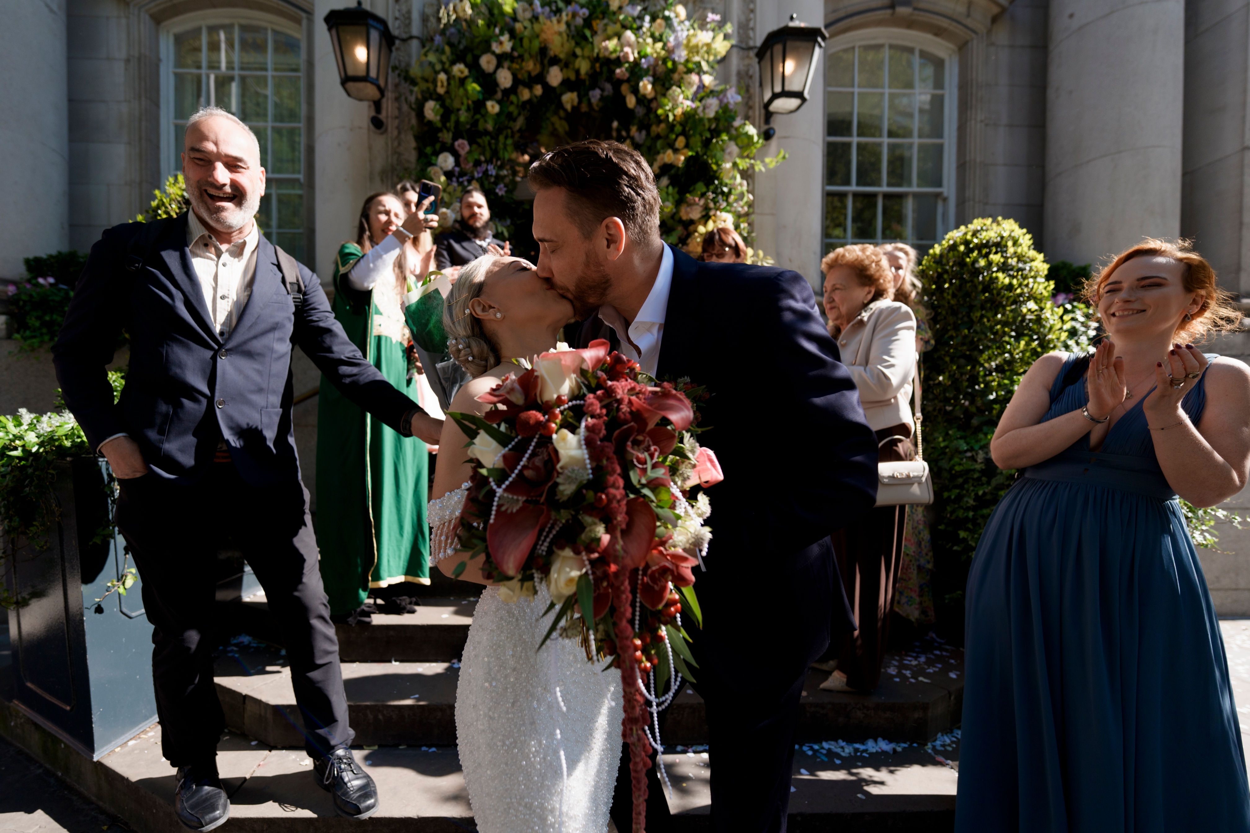 Joyful newlyweds share a passionate kiss on the town hall steps, cheered by guests.
