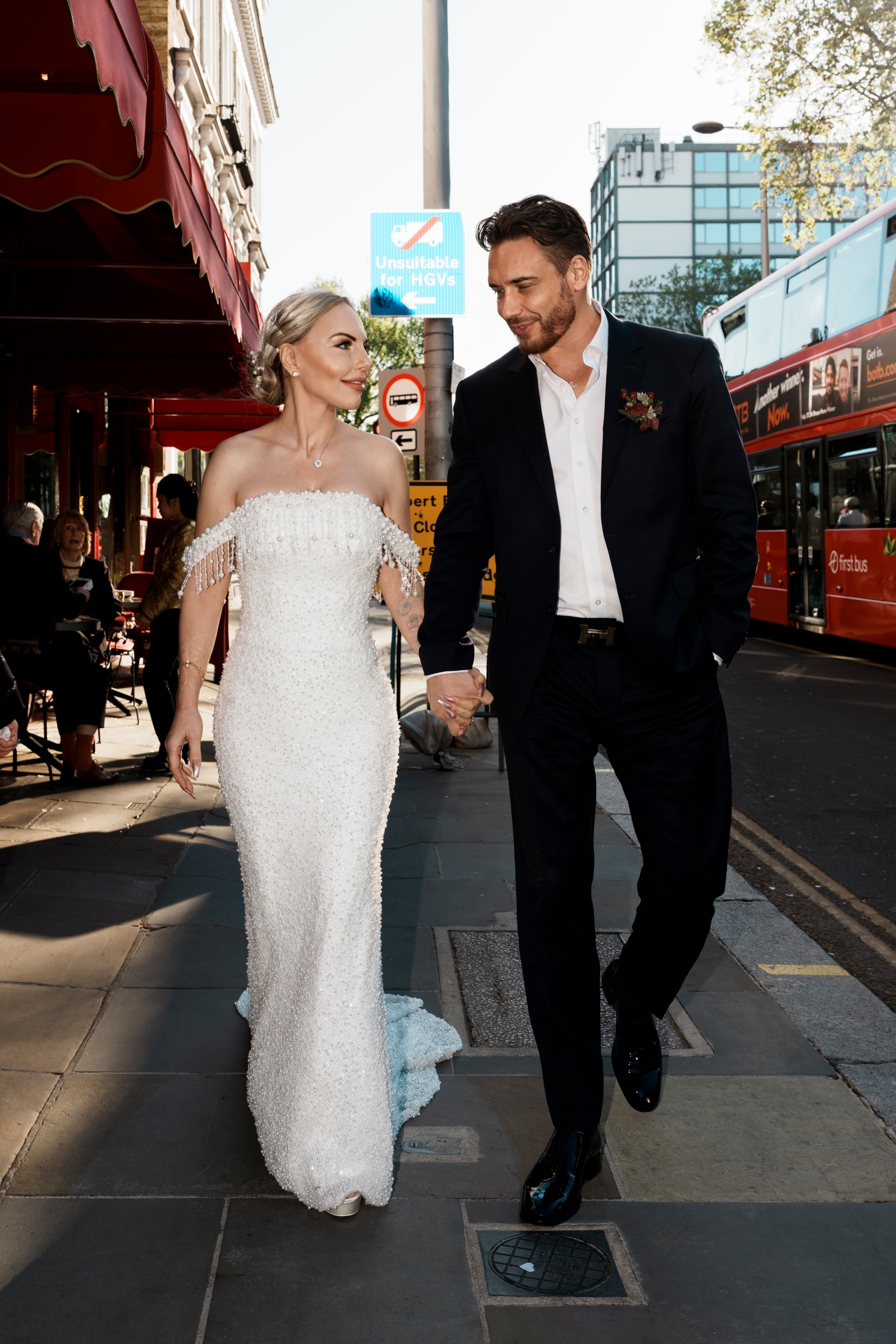 The stylish bride and groom share a loving glance strolling hand-in-hand.